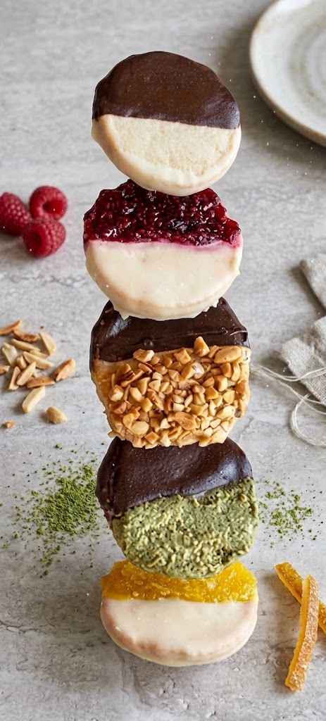 All five Brooklyn Black and White cookie flavors stacked together, surrounded by fresh raspberries, peanuts, matcha and candied orange peel